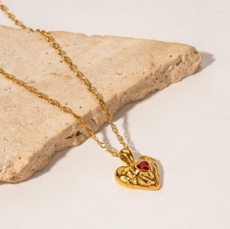 Diseño en forma de corazón de color dorado con detalle en rojo, delicado y combinable.