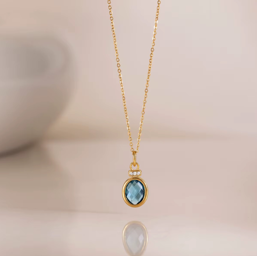 Diseño en forma de gota con dije de cristal azul ovalado y detalles brillantes.